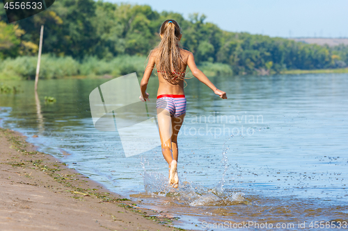 Image of Ten year old girl runs along the riverbank, view from the back