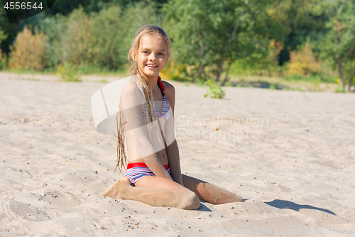 Image of Teen girl sits on a river sandy river beach