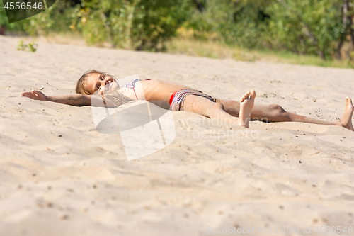 Image of Teen girl sunbathes alone on a river sandy river beach