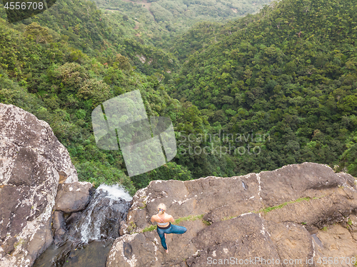 Image of Active sporty woman relaxing in nature, practicing yoga on high clif by 500 feet waterfall at Black river gorges national park on tropical paradise island of Mauritius