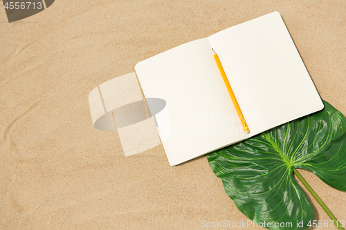 Image of notebook with pencil and leaf on beach sand