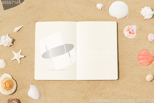 Image of notebook with seashells on beach sand