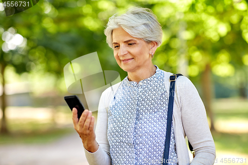 Image of happy senior woman with smartphone at summer park