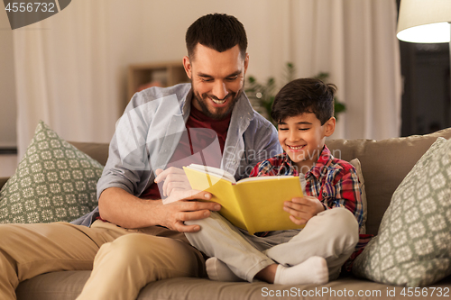 Image of happy father and son reading book sofa at home