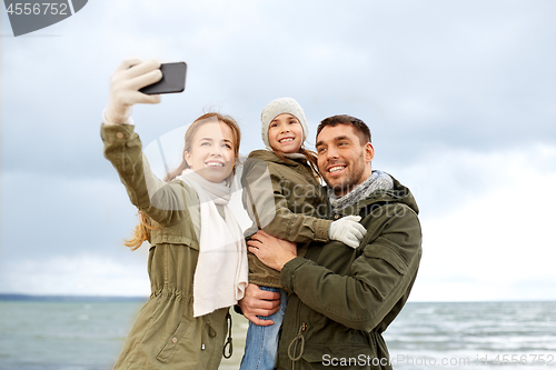 Image of family taking selfie by smartphone on autumn beach
