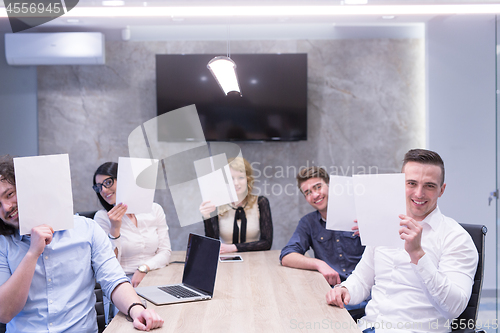 Image of startup business team holding a white paper over face