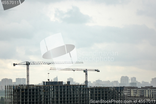 Image of Building under construction with two tower cranes against a gray cloudy sky. Photo from the drone.