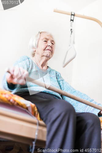 Image of Elderly 96 years old woman exercising with a stick sitting on her bad.