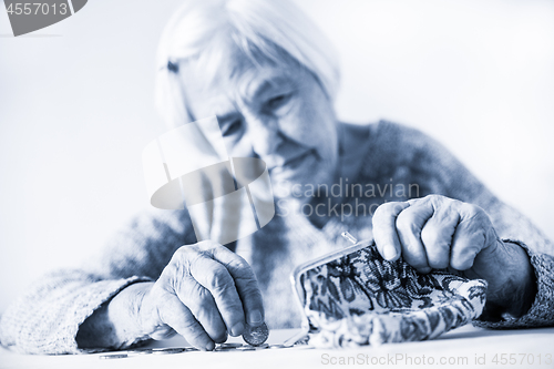 Image of Concerned elderly woman sitting at the table counting money in her wallet. Black and white blue toned image.