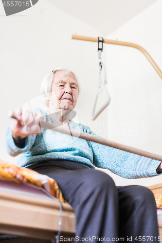 Image of Elderly 96 years old woman exercising with a stick sitting on her bad.