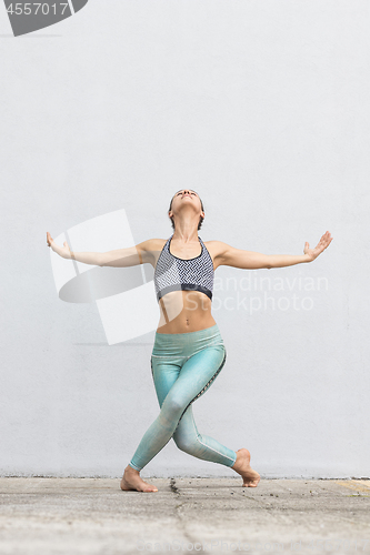 Image of Fit sporty active girl in fashion sportswear doing yoga fitness exercise in front of gray wall, outdoor sports, urban style