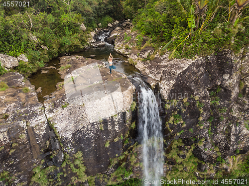 Image of Active sporty woman relaxing in nature, practicing yoga on high clif by 500 feet waterfall at Black river gorges national park on tropical paradise island of Mauritius