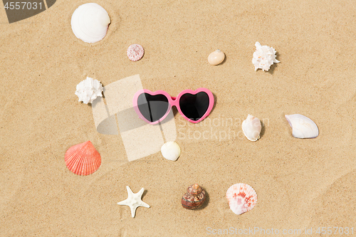 Image of heart-shaped sunglasses and shells on beach sand