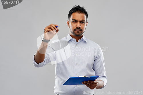 Image of strained indian businessman writing to clipboard