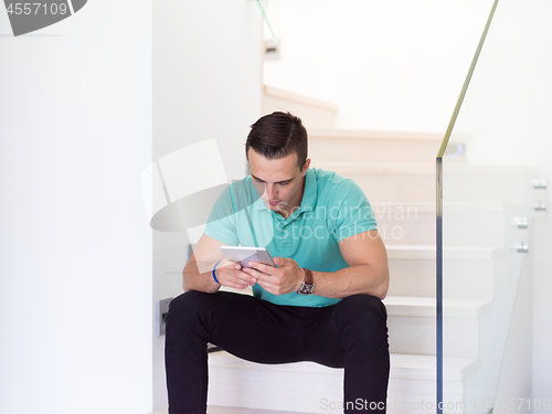 Image of man using a tablet while sitting on the stairs at home