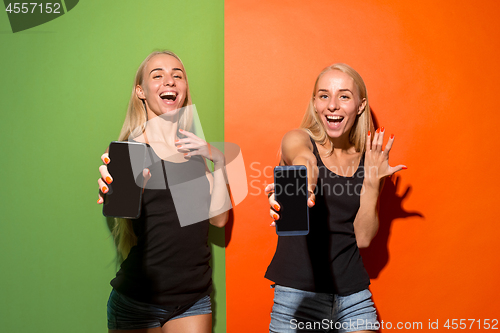 Image of Portrait of a confident casual girls showing blank screen mobile phone isolated over colorful background