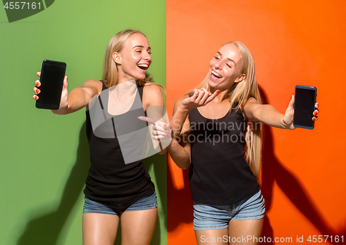 Image of Portrait of a confident casual girls showing blank screen mobile phone isolated over colorful background