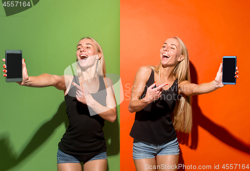 Image of Portrait of a confident casual girls showing blank screen mobile phone isolated over colorful background