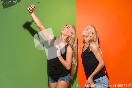 Image of Portrait of a happy smiling casual girls making selfie photo by mobile phone isolated over studio background