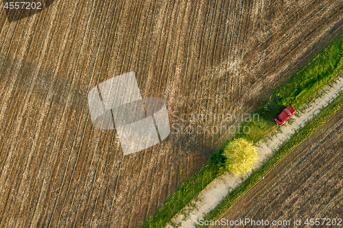 Image of Aerial view from the drone, a bird\'s eye view of agricultural fields with a road through and red car on it in the spring evening at sunset
