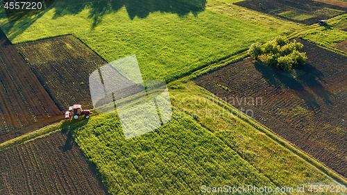 Image of Aerial view from the drone, a bird\'s eye view of agricultural fields with a road through and a tractor on it in the spring evening at sunset