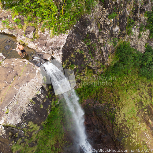 Image of Aerial top view of travel couple waving to drone, standing on the edge of 500 feet waterfall in the tropical island jungle of Black river gorges national park on Mauritius island