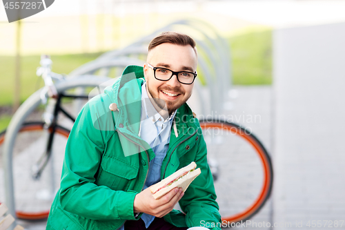 Image of happy young man or hipster with sandwich outdoors