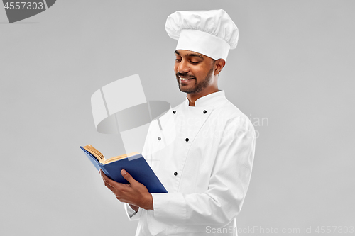 Image of happy male indian chef reading cookbook