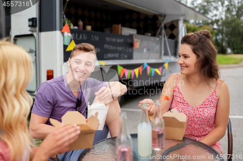 Image of happy friends with drinks eating at food truck