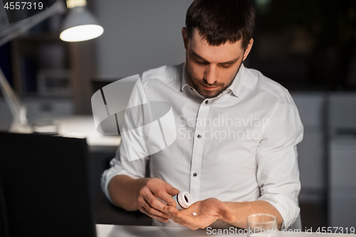 Image of businessman taking medicine pills at night office