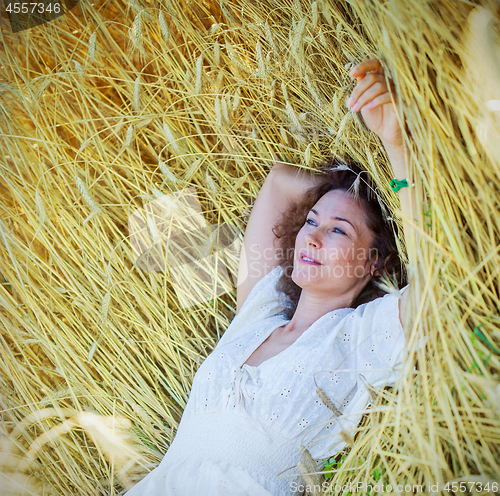 Image of beautiful woman lies among the ears of corn in the field
