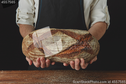 Image of Baker\'s hands hold an oval bread.