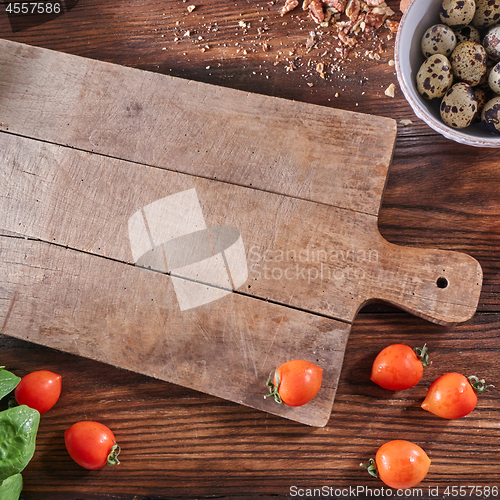 Image of Ripe tomatoes, quail eggs in a bowl and nut crumbs on a wooden board with a toe with an empty board and copy space. Salad preparation concep. Top view