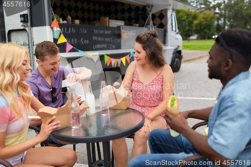 Image of happy friends with drinks eating at food truck