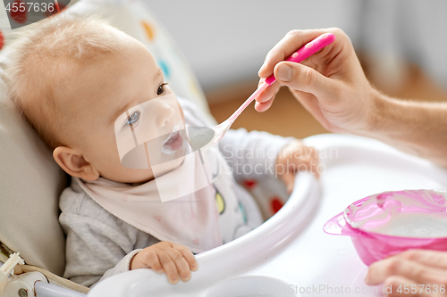 Image of father feeding baby sitting in highchair at home