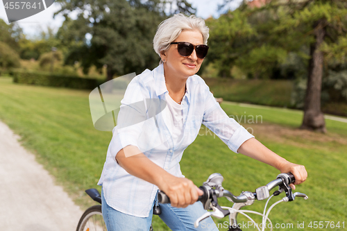 Image of happy senior woman riding bicycle at summer park