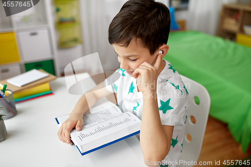 Image of student boy in earphones reading book at home