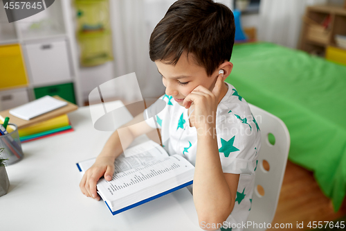 Image of student boy in earphones reading book at home