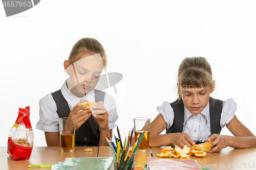 Image of Two tired schoolgirls at recess eat an orange and drink juice