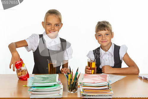 Image of Two school girlfriends drink juice and eat cookies at a table in a school class