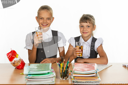 Image of Two funny schoolgirls at a table drink juice, and look in the frame