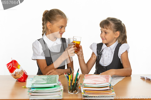 Image of Two funny schoolgirls at a table drink juice, and banged glasses