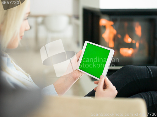 Image of young woman using tablet computer in front of fireplace