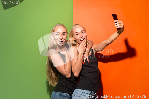 Image of Portrait of a happy smiling casual girls making selfie photo by mobile phone isolated over studio background