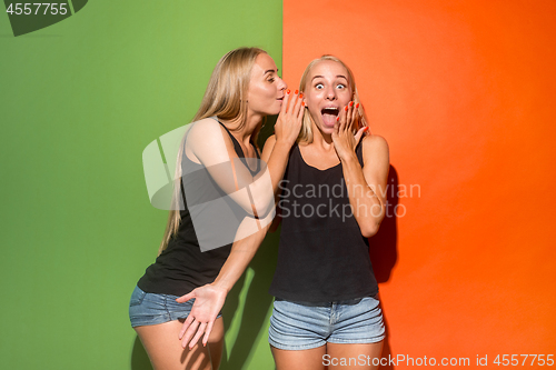 Image of The young woman whispering a secret behind her hand over studio background