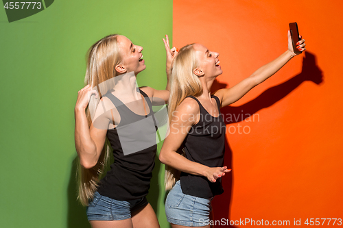 Image of Portrait of a happy smiling casual girls making selfie photo by mobile phone isolated over studio background