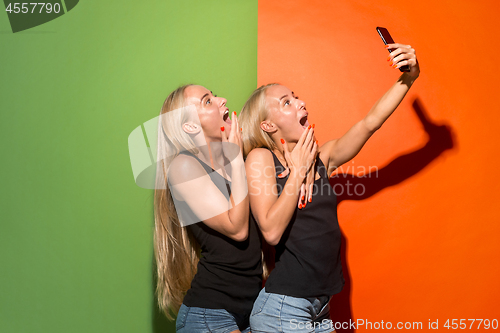 Image of Portrait of a happy smiling casual girls making selfie photo by mobile phone isolated over studio background