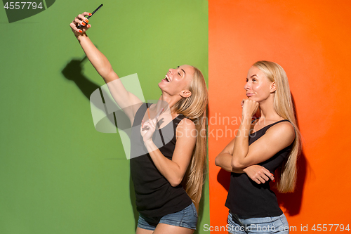 Image of Portrait of a happy smiling casual girls making selfie photo by mobile phone isolated over studio background