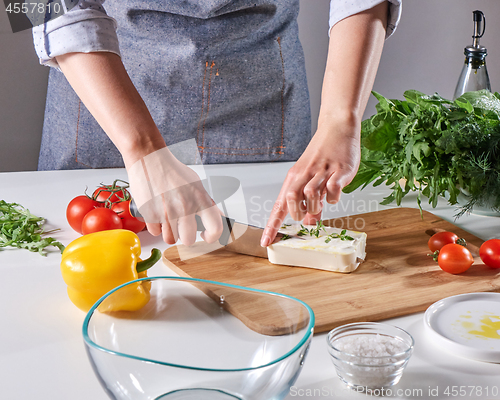 Image of Woman\'s hands cut the cheese with the sprouts on the wooden board on the kitchen table with different vegetables. Step by step cooking healthy salad