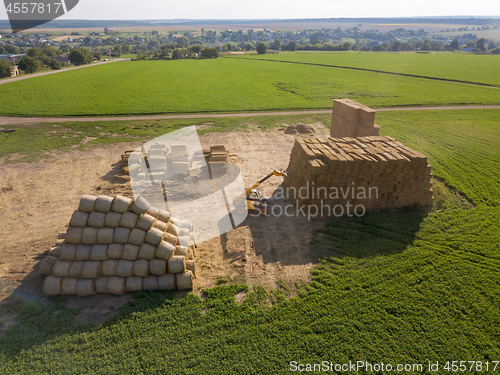 Image of Green field with haystacks and agricultural machine around blue sky on an autumn sunny day.